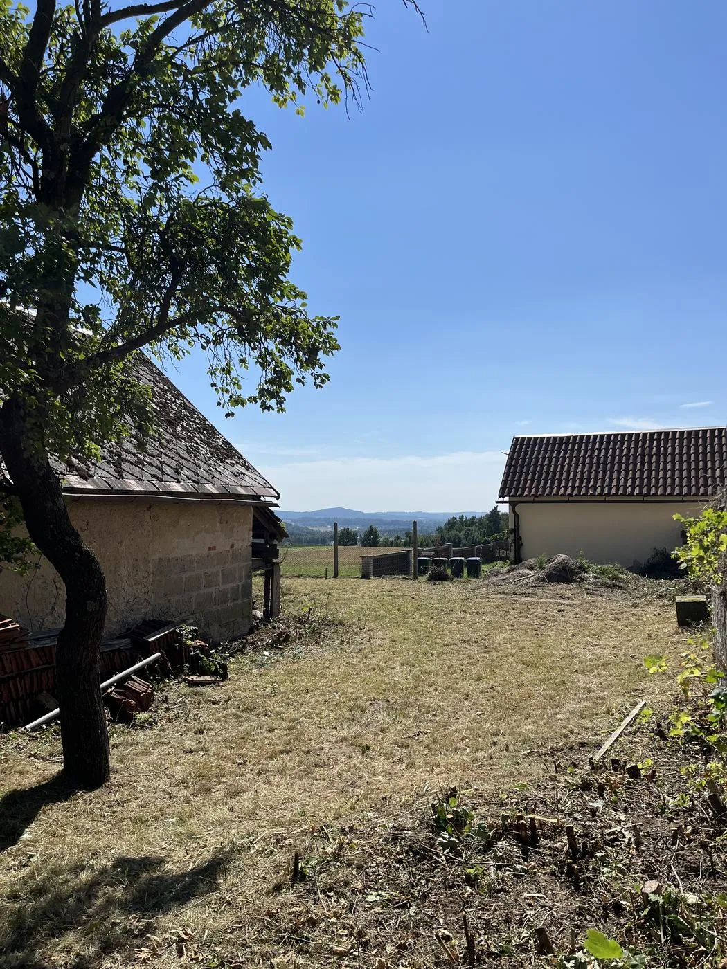 Stejné místo po posekání — čistý trávník až k sousednímu domu, v pozadí výhled do kraje